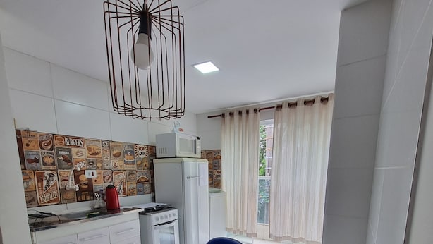 A modern kitchen with white cabinets, a wooden island, and a backsplash with food-themed tiles. - Studio in Butantã, near USP. (São Paulo)