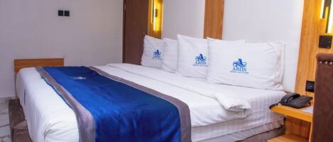 A hotel room with a bed, pillows with the hotel's logo, a bedside phone, and a wooden nightstand.