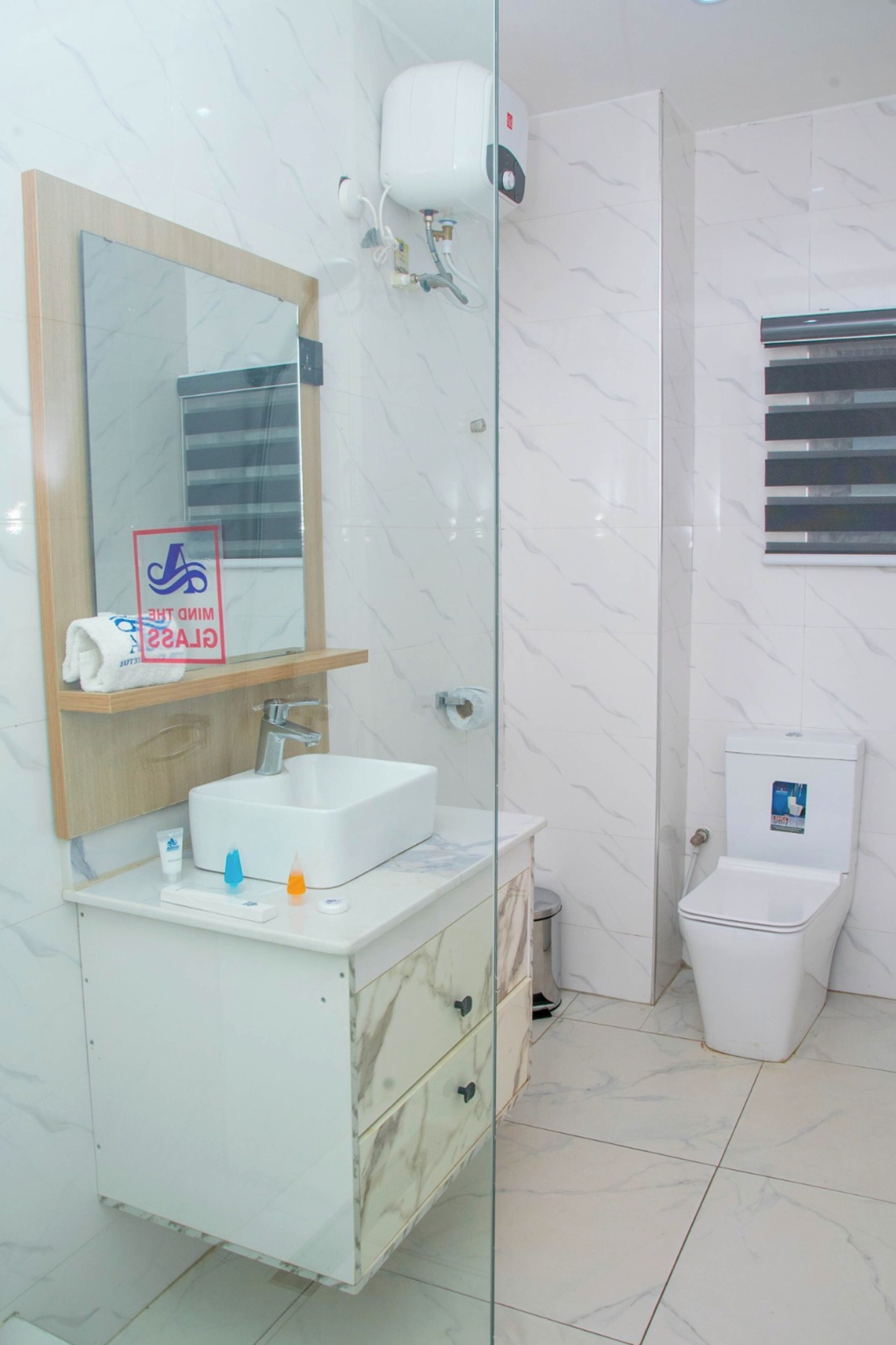 A bathroom with a marble sink, a glass shower enclosure, a toilet, and a mirror with a towel hanging on it.