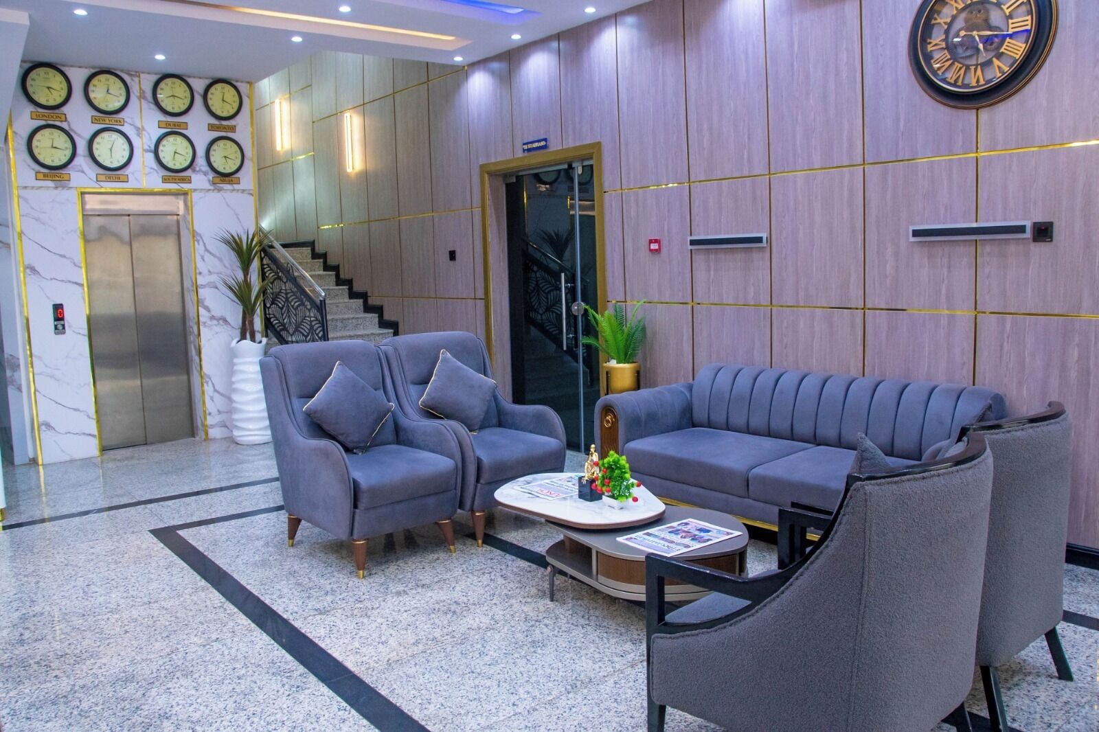 A lobby with two grey sofas, a coffee table, a clock, and a staircase.