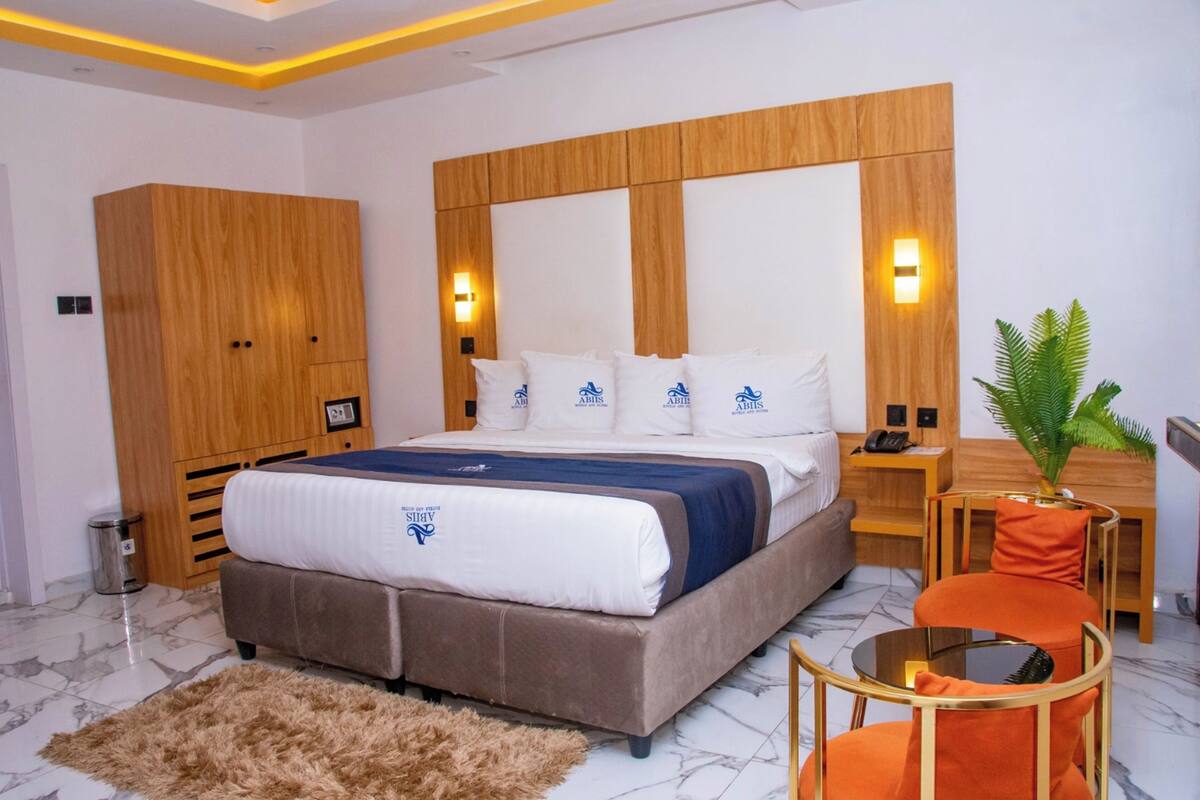 Une chambre d’hôtel moderne avec un grand lit, une armoire en bois et une petite table ronde agrémentée d’une plante.