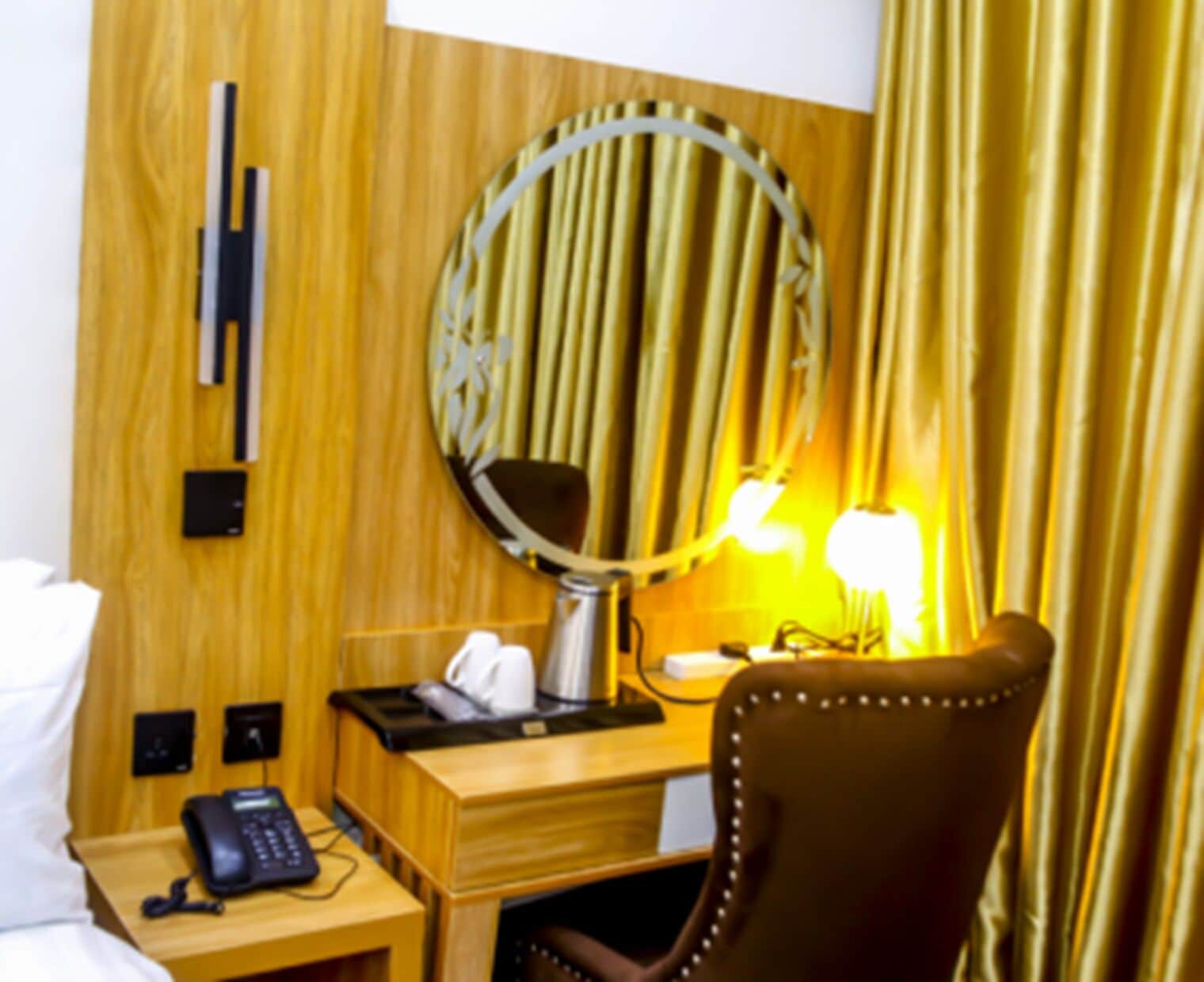 A hotel room with a wooden desk, a telephone, a lamp, and a mirror.