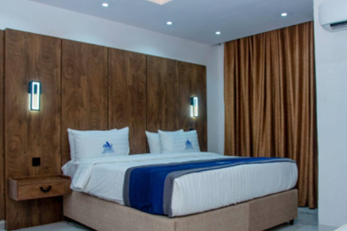 Une chambre moderne avec un grand lit, une tête de lit en bois, des tables de chevet et un rideau.