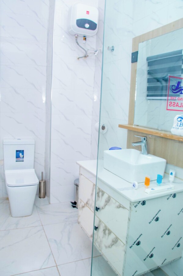 A bathroom with a glass shower enclosure, a white toilet, and a sink with toiletries.