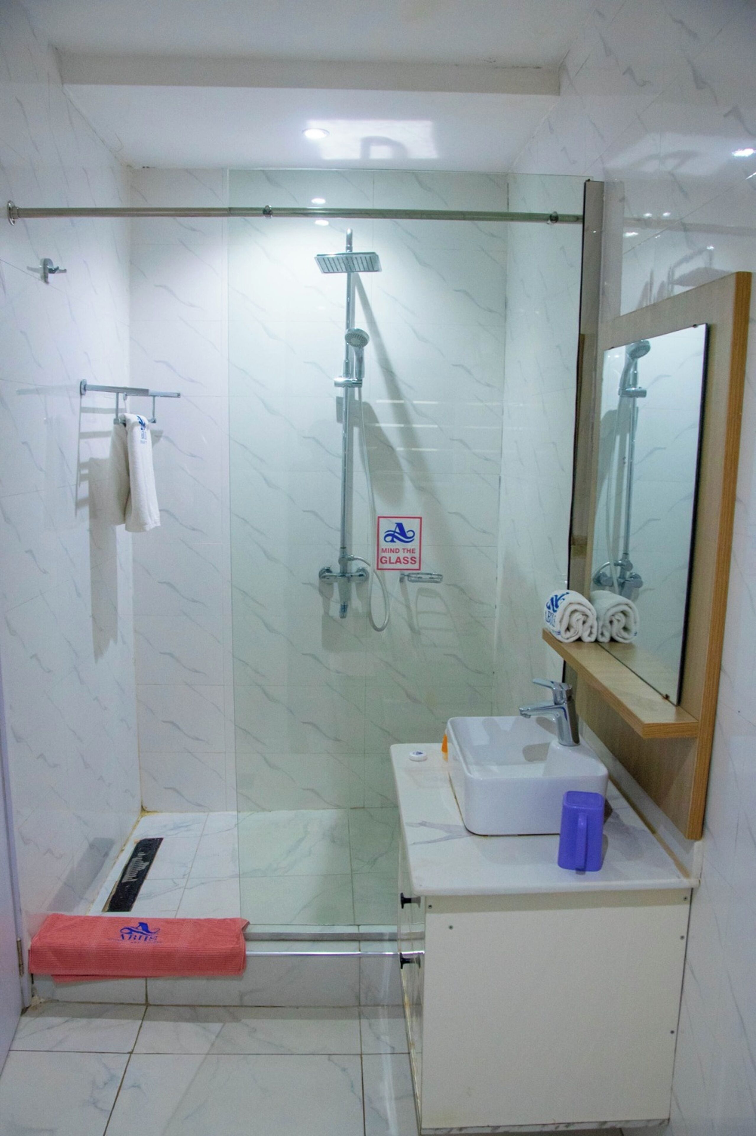 A bathroom with a glass shower enclosure, a sink with a mirror, and a towel rack.