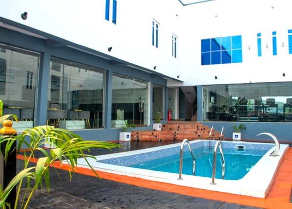 A modern building with large glass windows, a swimming pool, and a brick staircase leading to the entrance. - Abiis hotel &Suites (Abeokuta)