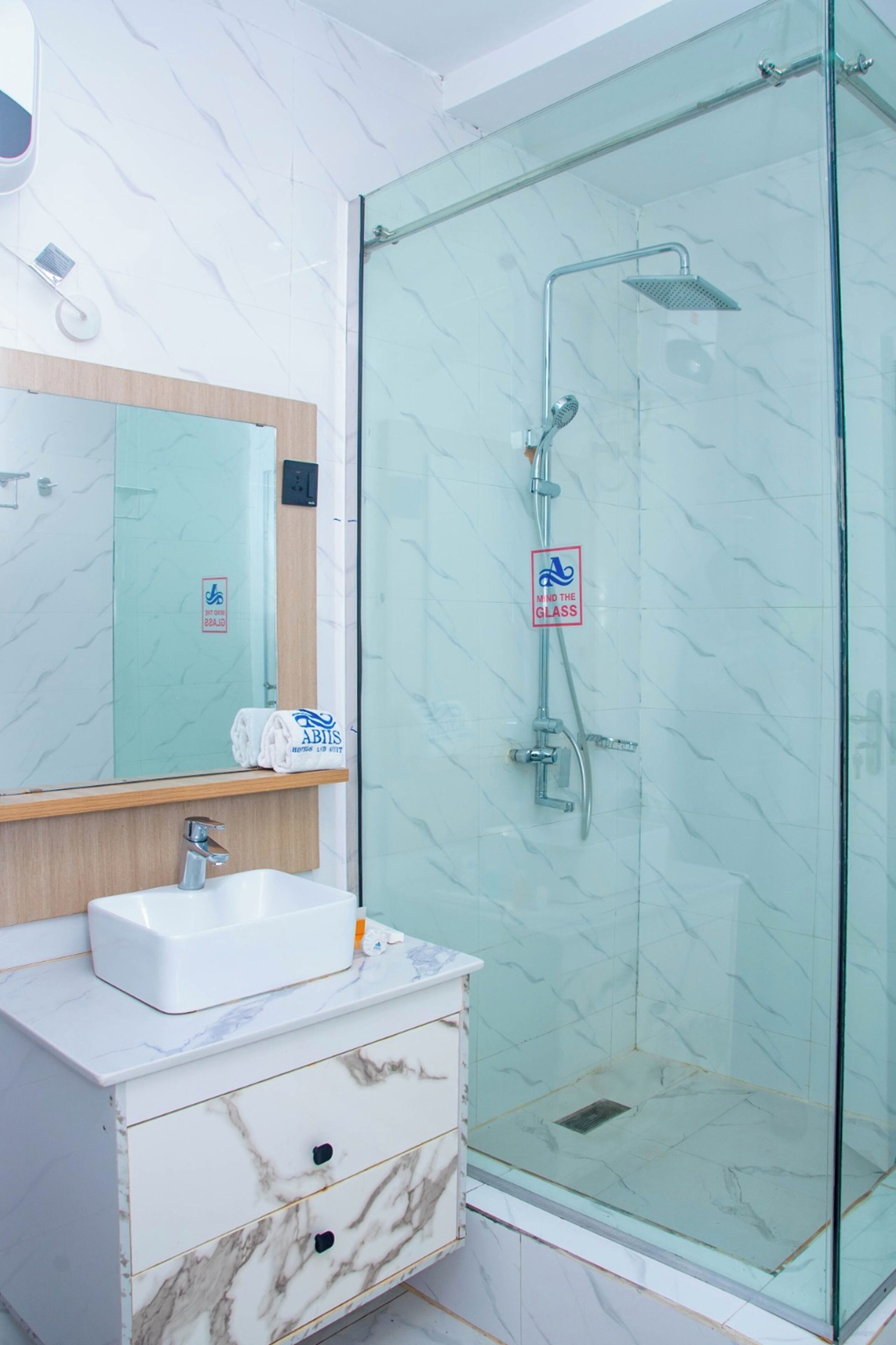 A bathroom with a glass-enclosed shower, a white sink with a marble countertop, and a mirror above the sink.