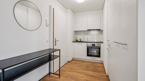 A compact kitchen with white cabinets, a black countertop, and a built-in oven. - Premium studio in city center - Color 3 (Zürich)