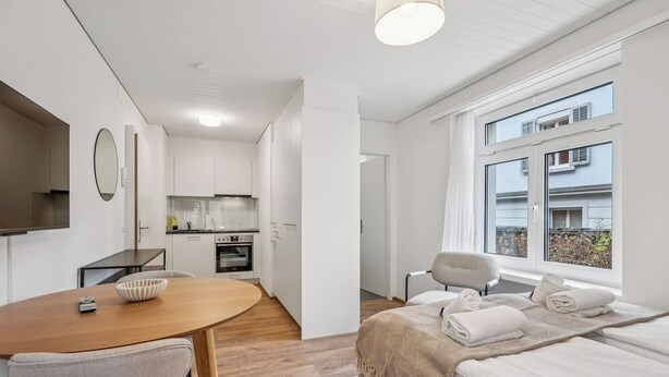 A compact, modern room with a kitchenette, a dining area, and a bed with a view of the outside. - Premium studio in city center - Color 3 (Zürich)