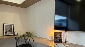 Une cuisine moderne avec un plan de travail en bois, deux chaises noires, un tableau encadré, une bougie allumée, une bouteille et un téléviseur à écran plat.