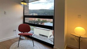 Une pièce avec une grande fenêtre, un fauteuil rouge, un tapis rond et une lampe de table.