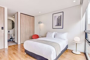 A modern hotel room with a large bed, a bedside table, a red chair, a floor lamp, and a framed picture on the wall. - w Beautiful Loft in the Heart of Bogot (Bogotá)