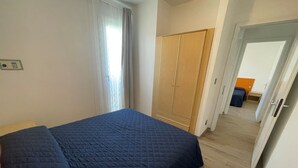 A bedroom with a bed, a wardrobe, and a door leading to another room. - Sunny Family Apartment Steps From the Beach (San Michele al Tagliamento)