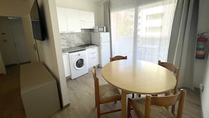 A compact kitchen with a washing machine, a microwave, and a stove. There is a dining table with chairs and a TV mounted on the wall. - Sunny Family Apartment Steps From the Beach (San Michele al Tagliamento)