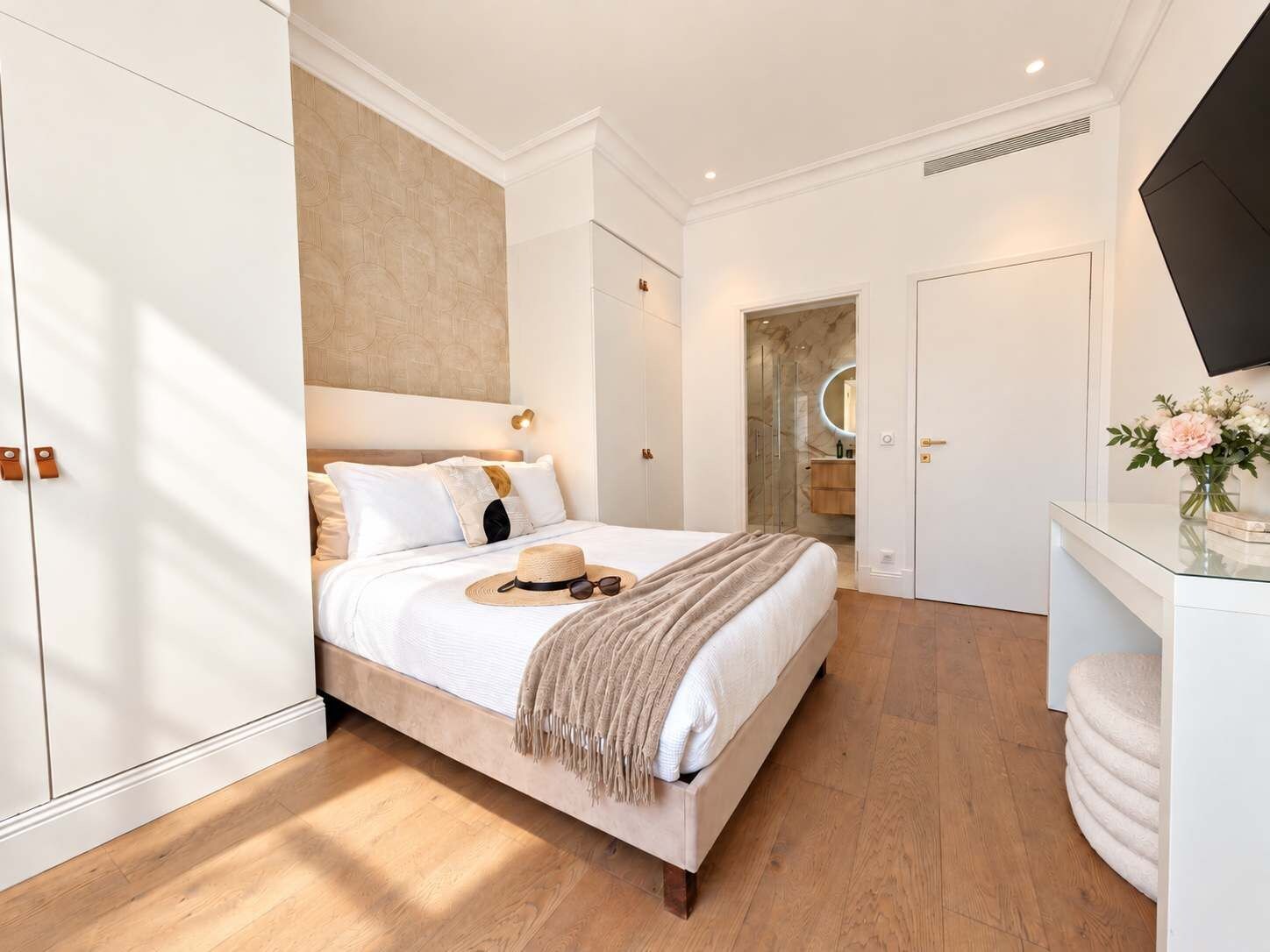 Een moderne slaapkamer met een groot bed, een kaptafel met spiegel en een flatscreen televisie aan de muur.