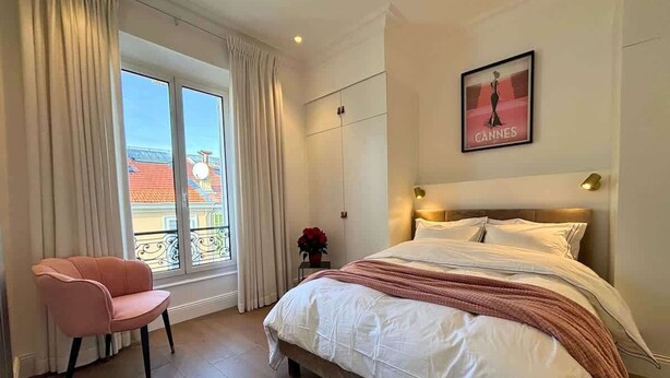 A bedroom with a bed, a chair, a window with curtains, and a framed picture on the wall. - Scarlett - 4 Bedroom next to the Croisette (Cannes)