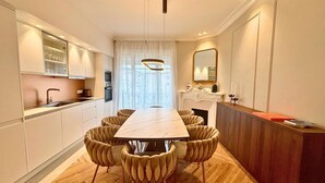 A modern kitchen with a dining area, featuring a marble countertop, a built-in oven, and a large window with curtains. - Scarlett - 4 Bedroom next to the Croisette (Cannes)
