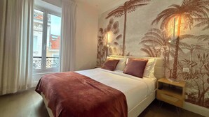 A hotel room with a bed, a nightstand, a window with curtains, and a wall with a tropical mural. - Scarlett - 4 Bedroom next to the Croisette (Cannes)