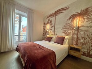 A hotel room with a bed, a nightstand, a window with curtains, and a wall with a tropical mural. - Scarlett - 4 Bedroom next to the Croisette (Cannes)