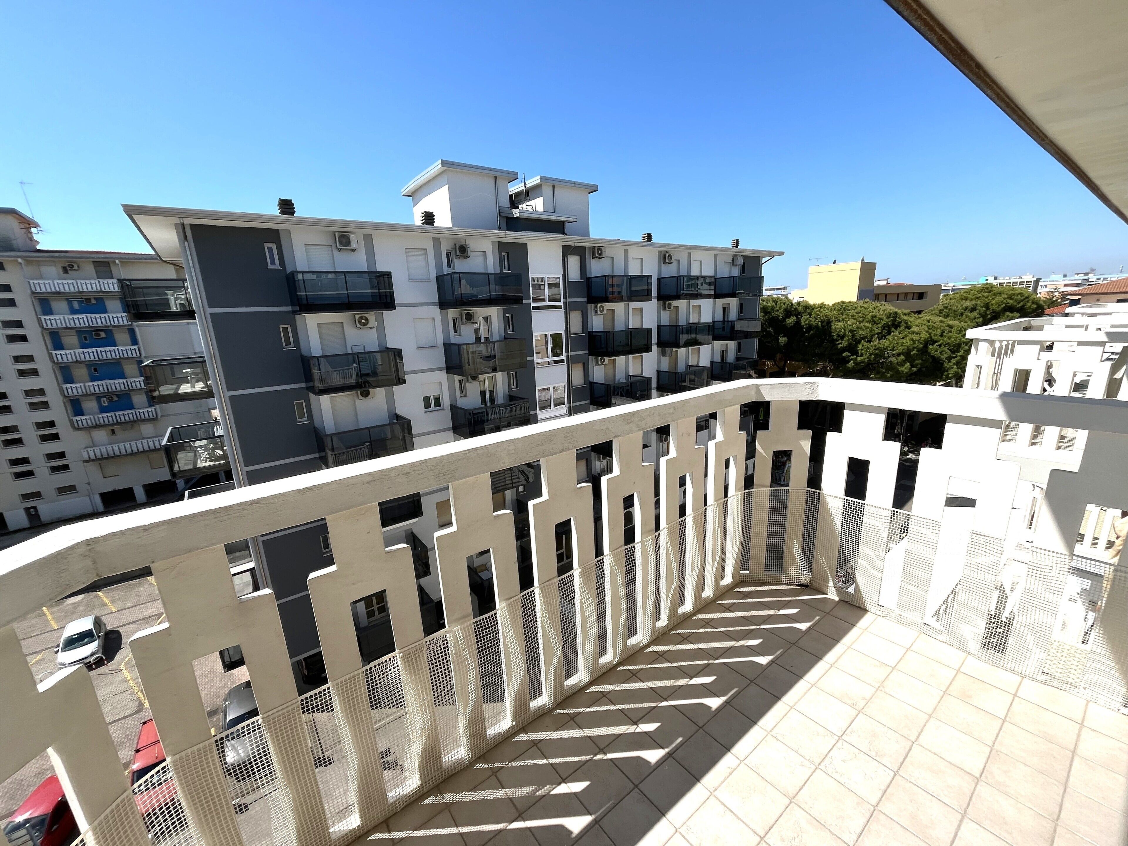 A balcony with a white railing and tiled floor, overlooking a residential area with multi-story buildings.