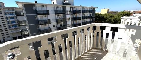 A balcony with a white railing and tiled floor, overlooking a residential area with multi-story buildings.