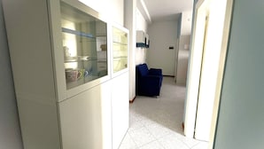 A narrow hallway with a kitchenette on the left, a blue sofa in the center, and a door leading to another room on the right. - Comfortable House Close to the Beach in Bibione (San Michele al Tagliamento)