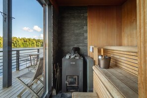 A sauna with a stone wall, a wooden bench, and a view of the lake.