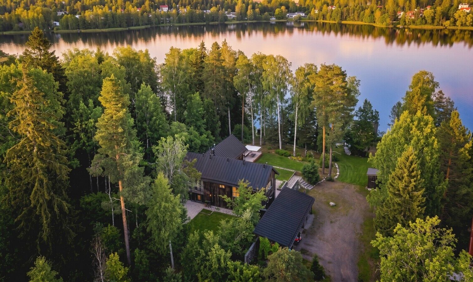 Eine Blockhütte am Seeufer mit einer großen Terrasse, umgeben von dichtem Wald und einem stillen See.