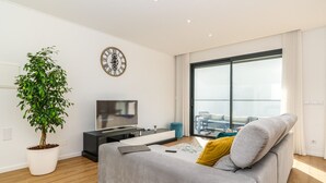 A modern living room with a large window, a flat-screen TV, a grey sofa, and a potted plant. - Scandinavian Minimalist Villa • BBQ • Gym • Kids Area • Table Tennis (Câmara de Lobos)