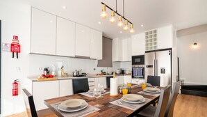 A modern kitchen with white cabinets, a wooden dining table set for four, and a hanging light fixture. - Scandinavian Minimalist Villa • BBQ • Gym • Kids Area • Table Tennis (Câmara de Lobos)