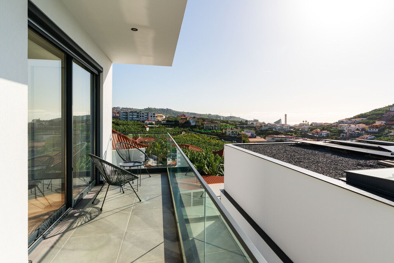 A balcony with a glass railing, a chair, and a table.