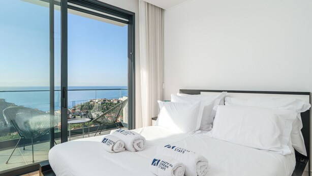 A hotel room with a large bed, a view of the sea, and a balcony with a chair. - Scandinavian Minimalist Villa • BBQ • Gym • Kids Area • Table Tennis (Câmara de Lobos)