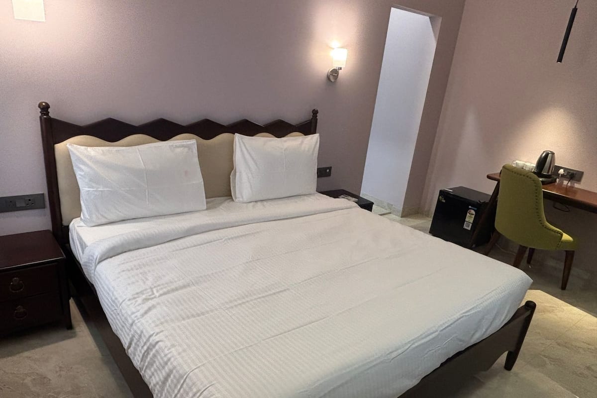A neatly made bed with a wooden headboard and two pillows, a desk with a chair, and a wall-mounted light fixture.