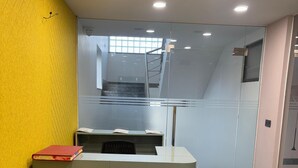 Bancada de recepção com divisória de vidro, escada ao fundo e parede amarela.