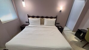 Uma cama bem arrumada com lençóis brancos, uma cabeceira de madeira escura e duas mesas de cabeceira com abajures.