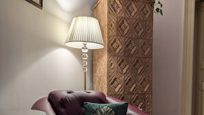 Une pièce comprenant un fauteuil en cuir, une commode à motifs, une lampe et une estampe botanique encadrée accrochée au mur.