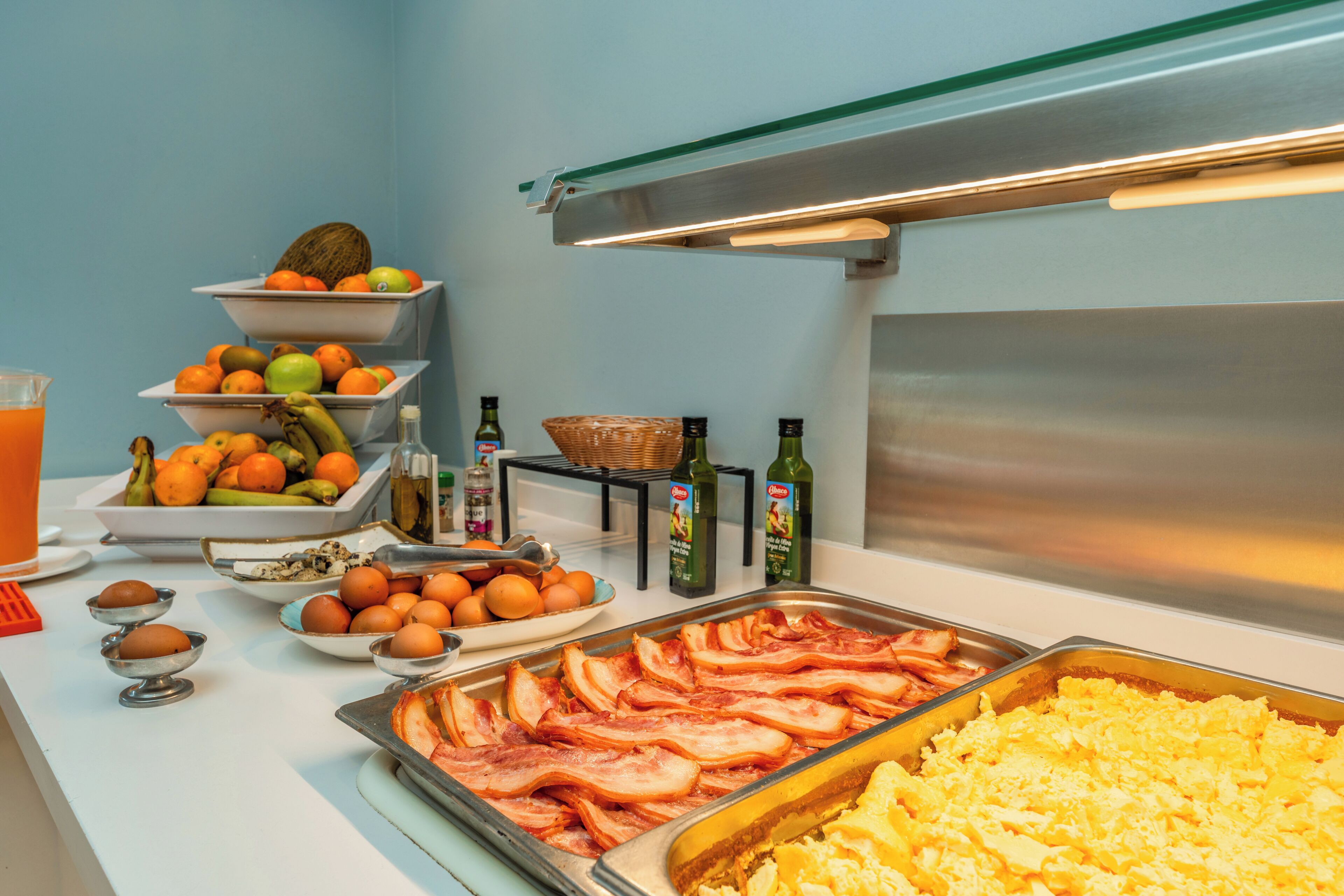 Un bufé con diversas opciones de comida, incluyendo tocino, huevos, naranjas y plátanos.