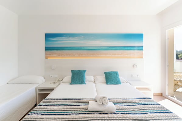 Une chambre d’hôtel avec un lit, deux tables de chevet, un téléphone et un tableau représentant une plage.