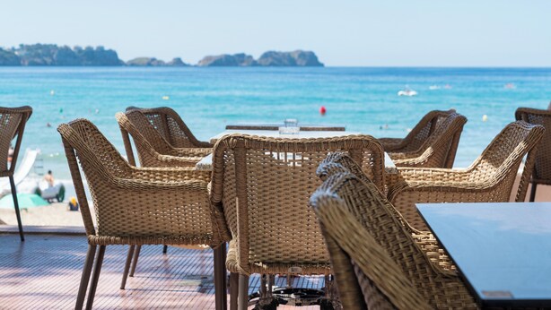 Rotan stoelen en een tafel op een terras met uitzicht op zee en verre eilanden.