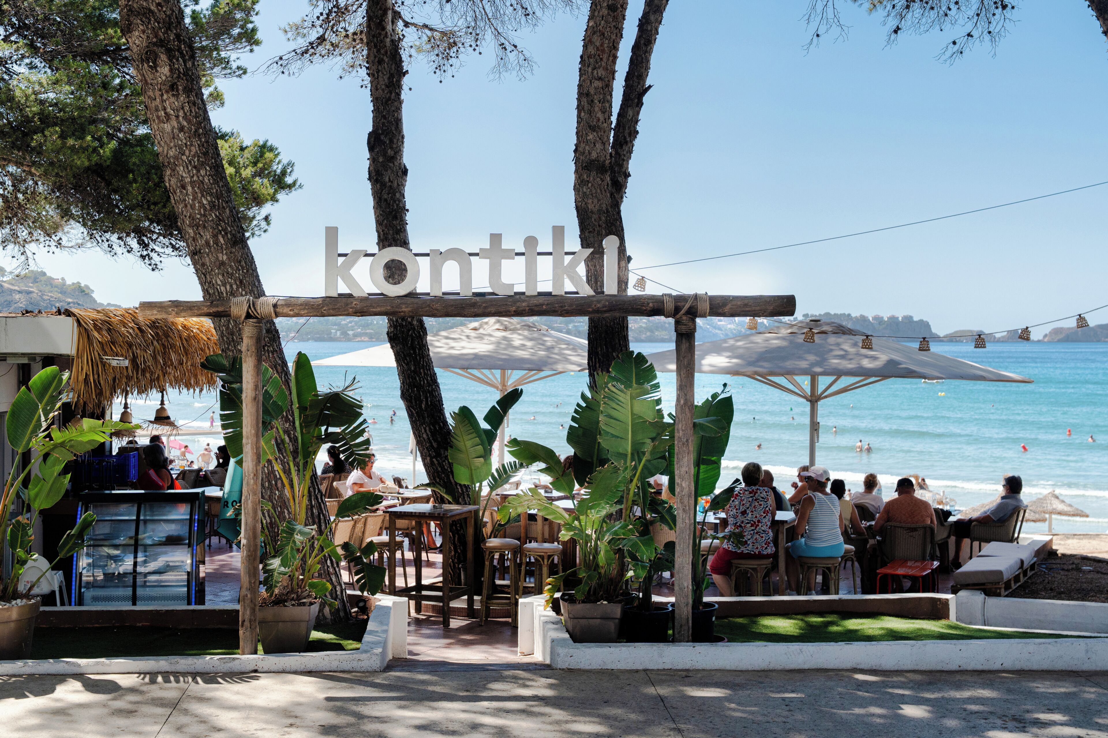 Un restaurante frente al mar con terraza, techo de paja y vista al océano.