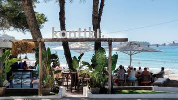 Un restaurante frente al mar con terraza, techo de paja y vista al océano.