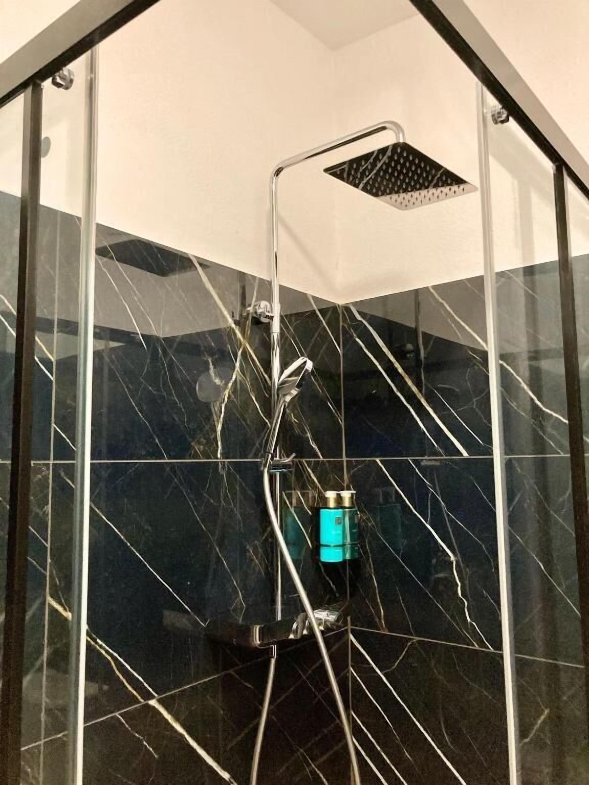Ducha con cerramiento de vidrio, ducha de lluvia y ducha de mano.