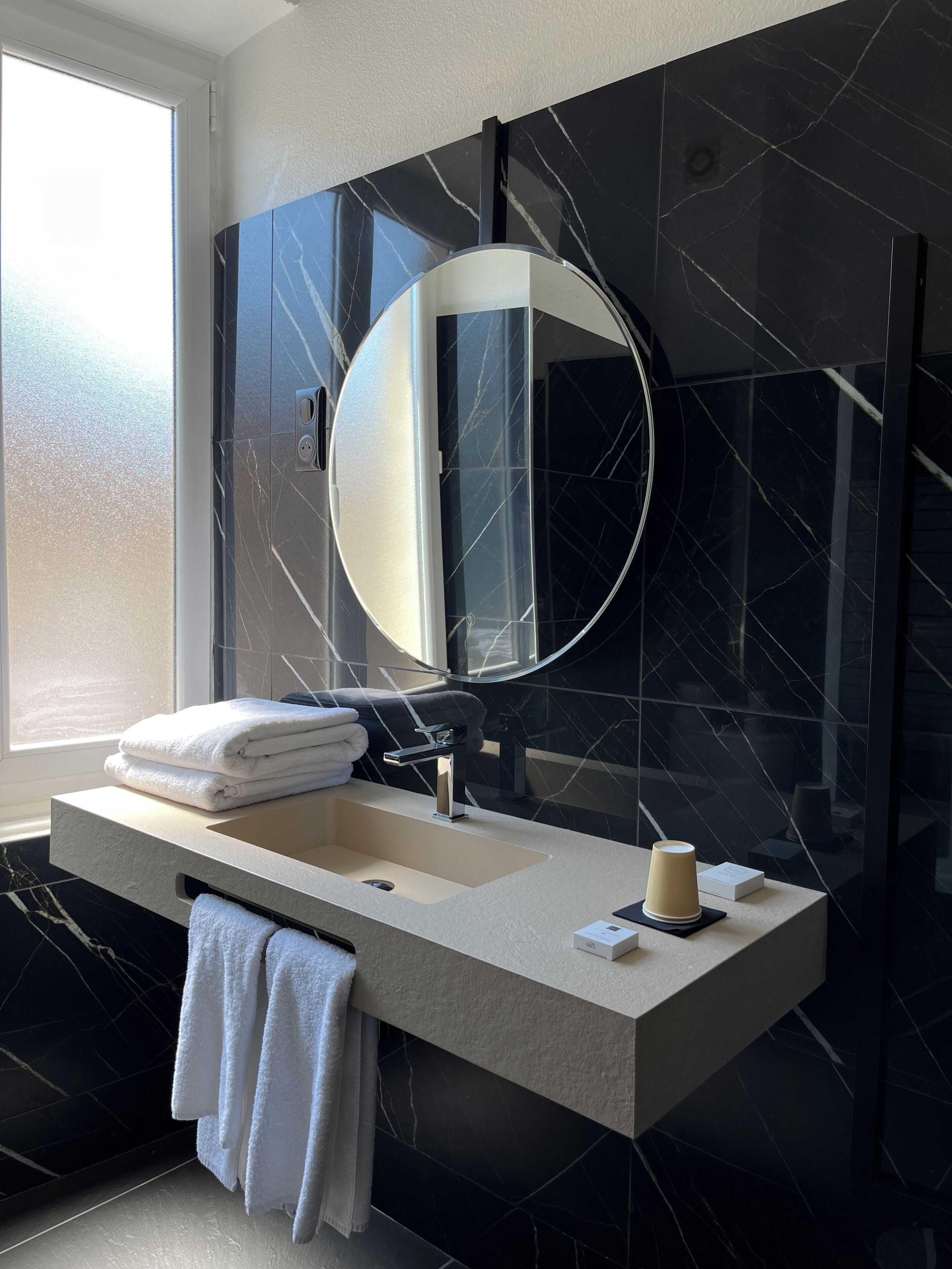A modern bathroom with a large mirror, a sink, and a window.