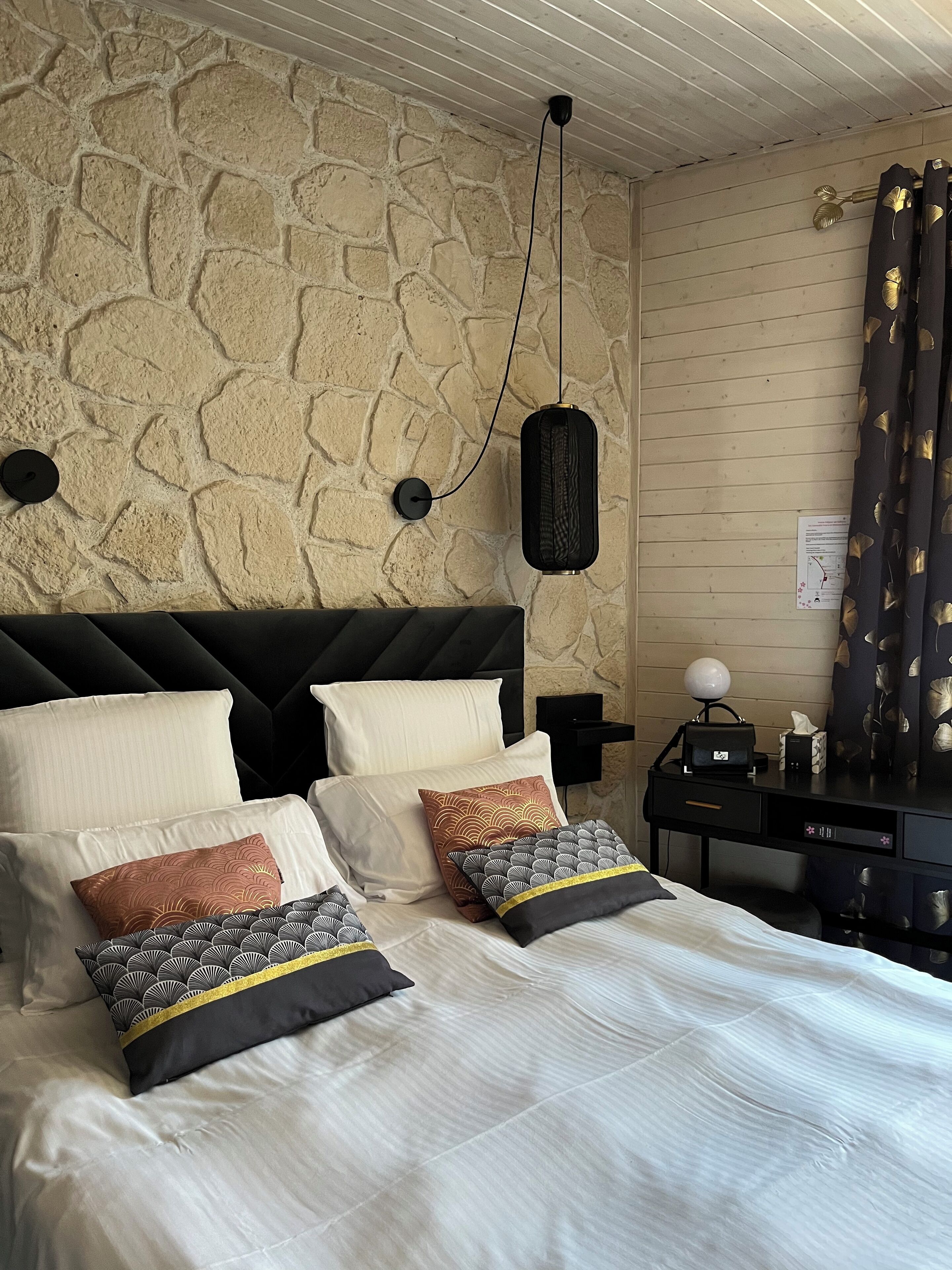 A bedroom with a stone wall, a black headboard, and a bed with multiple pillows.