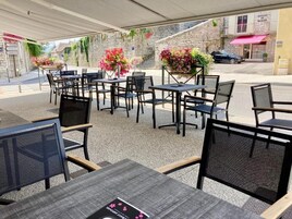 Um café ao ar livre com mesas e cadeiras, cercado por um muro de pedra e plantas em vasos.