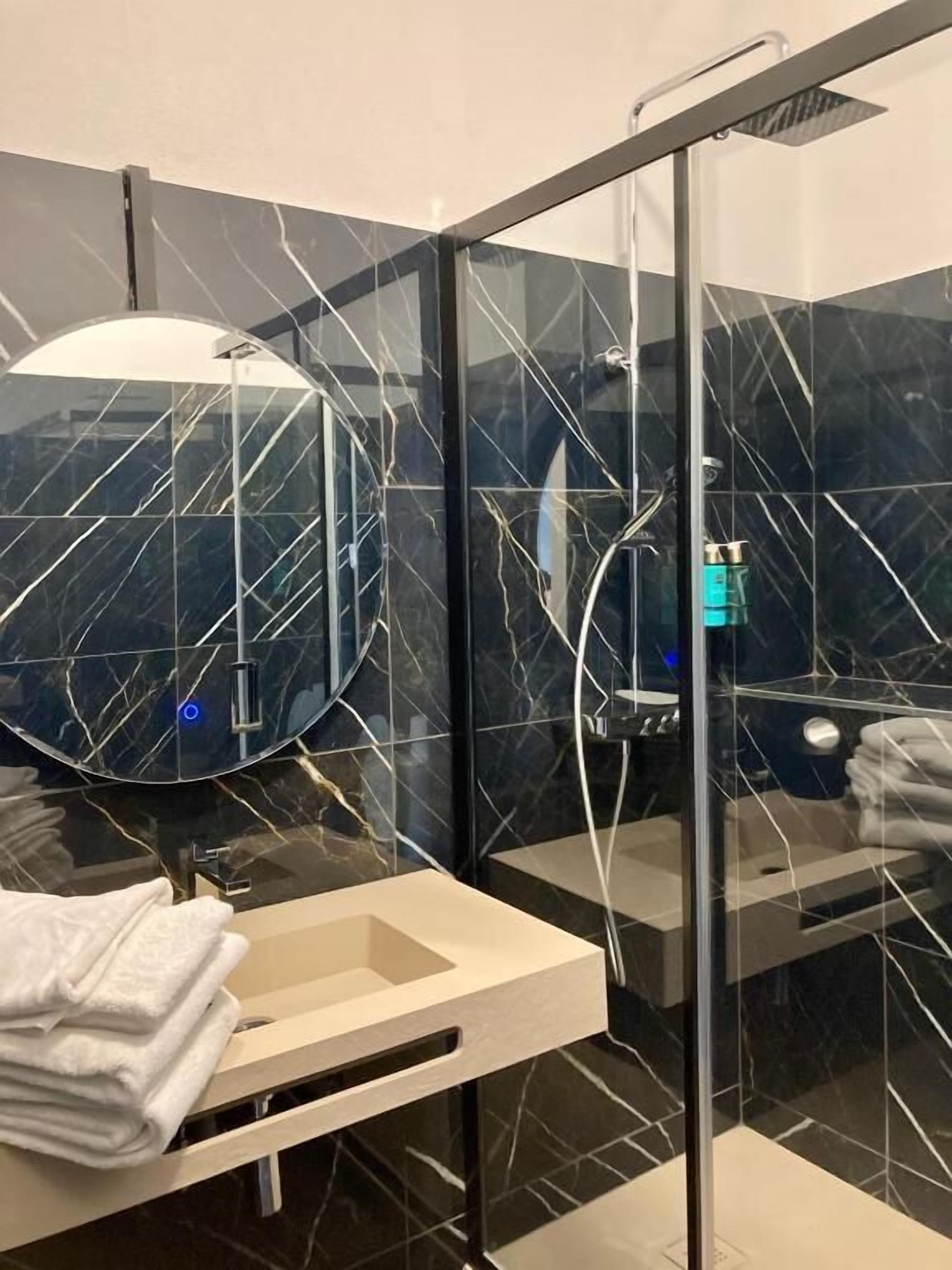 Un bany modern amb una cabina de dutxa de vidre, un mirall rodó i un lavabo blanc.
