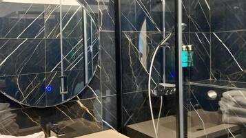 Un bany modern amb una cabina de dutxa de vidre, un mirall rodó i un lavabo blanc.