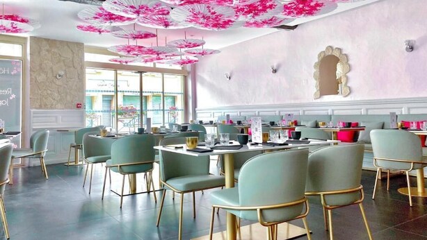 A restaurant with round tables and chairs, pink floral ceiling decorations, and a view of the outdoors through large windows. - Hôtel Le Sakura  (Morestel)