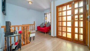 Un salon avec un canapé rouge, une table en bois ornée d’une statue et une porte-fenêtre coulissante.