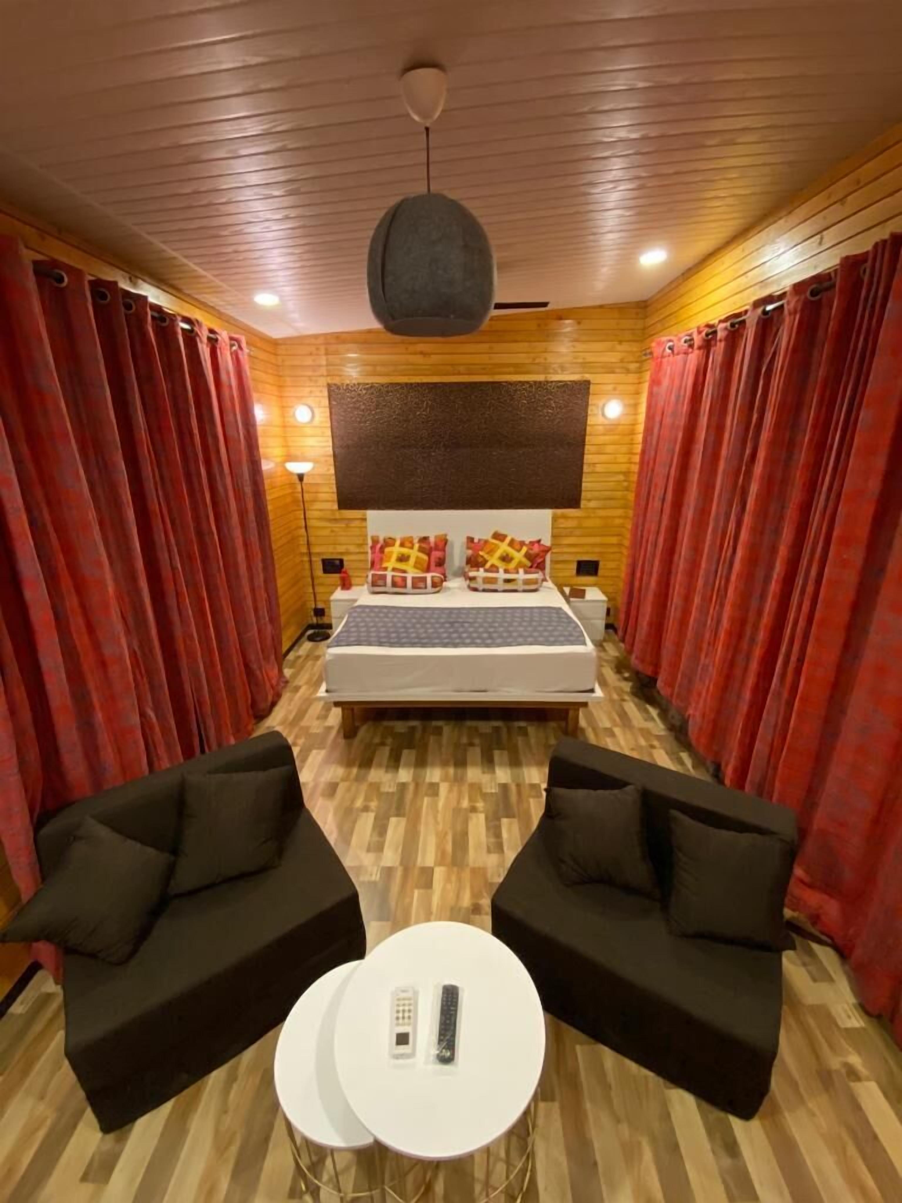 Una habitación de hotel con una cama, dos sofás negros, una mesita blanca y una lámpara en el techo.